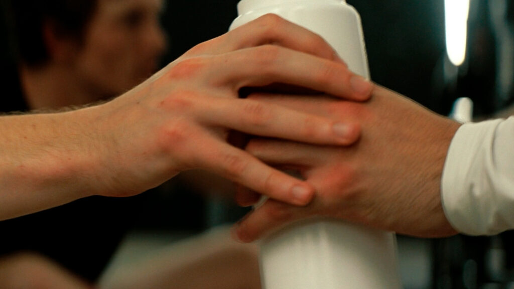 Heated Rivalry | cena de duas mãos masculinas se tocando enquanto passam uma garrafa de água para outro | Dandy Souza