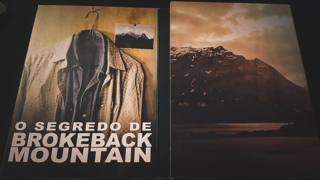 Encarte do Dvd O Segredo de Brokeback Mountain | À esquerda foto de duas camisas dividindo uma cruzeta — a de cime é de xadrez cor creme, a de baixo cor azul jeans. À Direita a foto de uma Montanha | Dandy Souza
